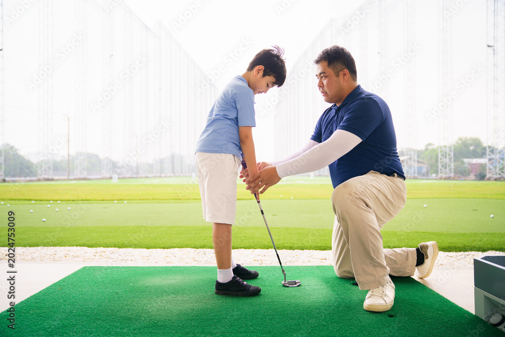Obraz premium Young boy practicing golf swing with professinoal golf instructor at driving range