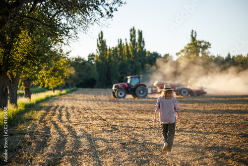Farmer observing agriculture process on field while tractor prepares soil with seeding machine for sowing seeds. Agricultural activity at farm