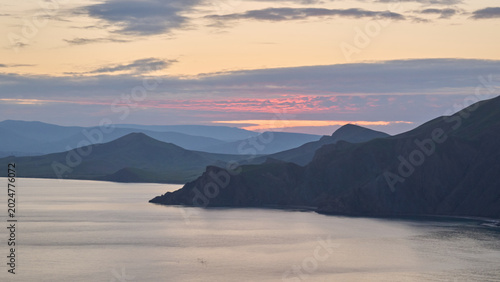 Fotografie Mountain coastline at sunset over calm sea