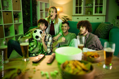 Young friends celebrating watching football on sofa at home