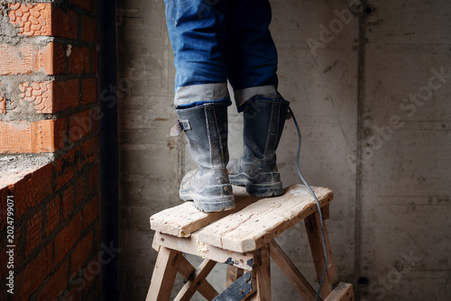 Foto Detail view of a construction worker wearing heavy-duty safety boots while working on a wooden stepladder inside an unfinished building