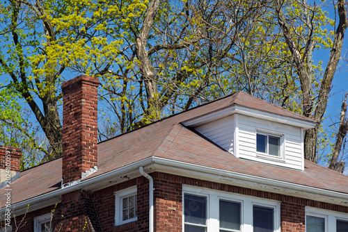 Fotografía Traditional brick house roof with a prominent chimney and a white hipped dormer
