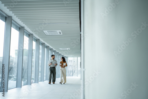 Canvas-taulu Business colleagues walking and conversing in modern office hallway