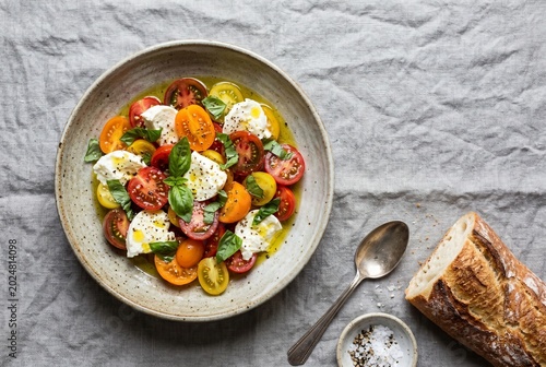 Fresh Caprese salad with colorful cherry tomatoes, mozzarella cheese, and basil in a ceramic bowl on a linen background