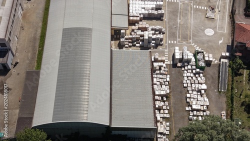 Aerial View of Industrial Warehouse and Storage Yard: An expansive industrial warehouse with a large, modern roof sits adjacent to a bustling storage yard filled with pallets of goods.