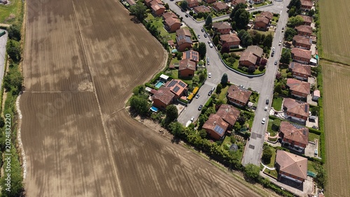 Aerial View of Suburban Homes: An aerial perspective showcases a cluster of suburban houses nestled beside a vast, tilled agricultural field.