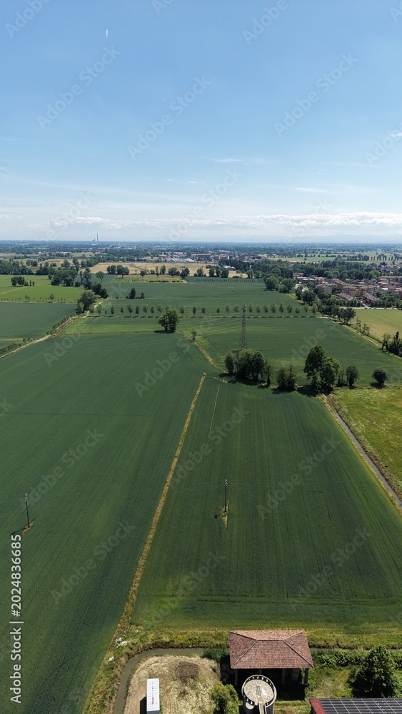 Obraz premium Panoramic Landscape of Rural Farmland: An expansive aerial view showcases a vast expanse of vibrant green farmland under a clear blue sky, dotted with trees and a small building.