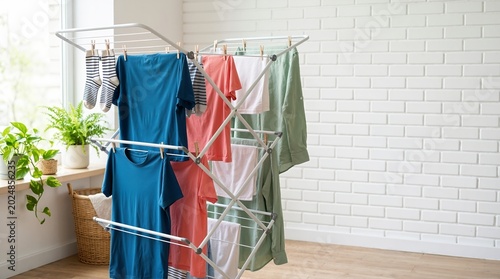 Colorful laundry hanging on a collapsible drying rack indoors. Wet clothes drying on a white metal stand in a bright room. Domestic housework concept