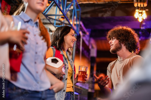 Fényképezés Young sports fans talking and holding beer during halftime of a soccer match in a pub