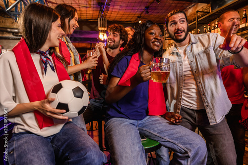 Cheerful football fans chatting at a pub bar counter before the match kicks off.