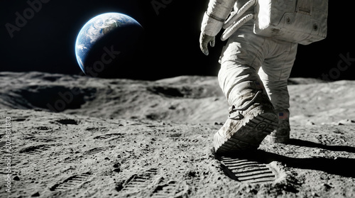 An astronaut walks on the moon's surface. The footprints are clear as Earth hangs in the dark sky. This scene shows exploration and achievement in space travel