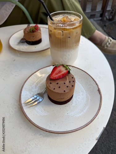 Top view of chocolate mousse desserts with fresh strawberries and iced coffee on a minimalist cafe table, featuring elegant plating and cozy brunch atmosphere.