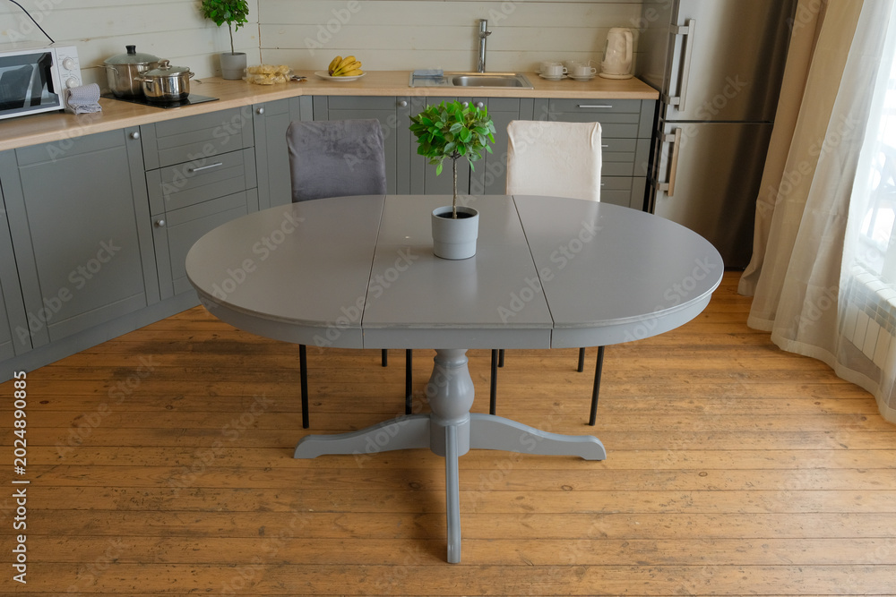 Fototapeta premium Dining room interior. Gray oval dining table, wood flooring, grey cabinets. Interior design of stylish kitchen with family table, modern chairs. Wooden floor. White wall. Template. New Luxury Home.