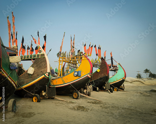 Row of colorful traditional wooden moon fishing boats with flags parked on sandy beach, beautiful tropical maritime heritage tourism landscape background.