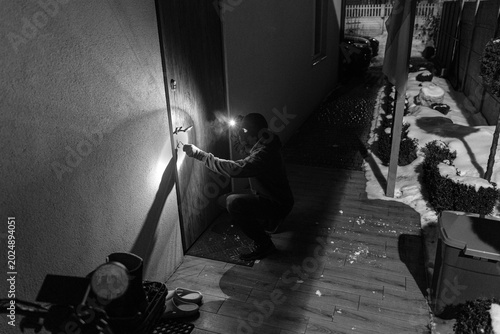 Canvastavla Man kneeling outside building at night, trying to unlock the door of house, abov