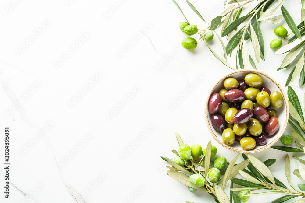 Naklejka premium Olives in wooden bowl and fresh olive tree branch at white background.