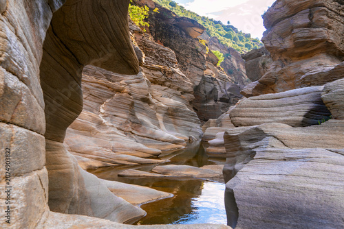 Narrow canyon with layered rock formations and small stream flowing through eroded stone landscape. Natural geological scenery shaped by water erosion in remote wilderness area