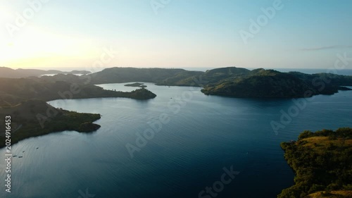 Wide drone shot of beautiful blue sea bays and green rolling hills at sunset in Riung 17 Islands National Park, Flores.
