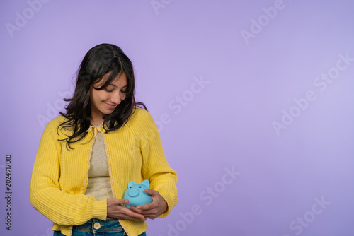 Young woman saving money holding blue piggy bank