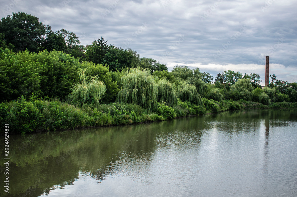 Fototapeta premium Calm lake surrounded by green trees under dramatic cloudy sky