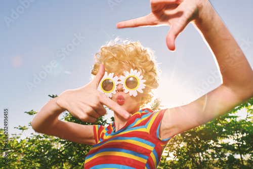 Картината върху платно A retro lifestyle outdoors scene captures a playful, colorful portrait of a person wearing sunglasses in bright daylight, conveying whimsy and bold fashion in a sunny, candid moment