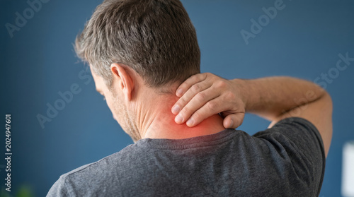 Adult man experiencing acute neck pain touching his sore neck an