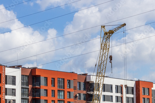 Fotografi Construction Crane Stands Tall Next to New Buildings Under Blue Sky With Clouds