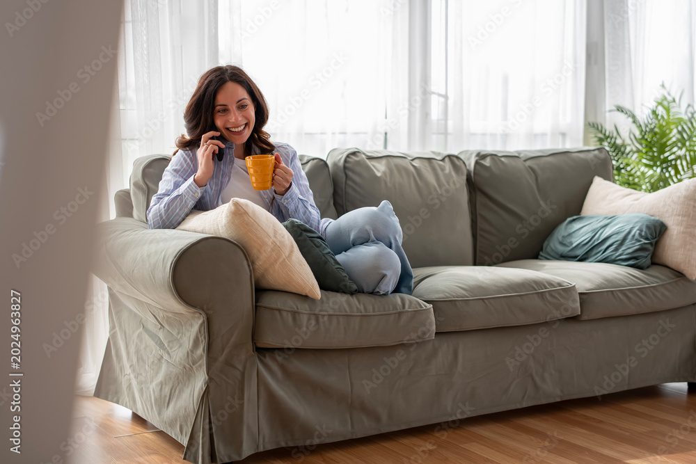 Fototapeta premium Happy woman talking on phone enjoying coffee at home
