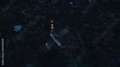 Aerial top view of a grand mosque illuminated at night surrounded by dark residential village houses in evening dawn