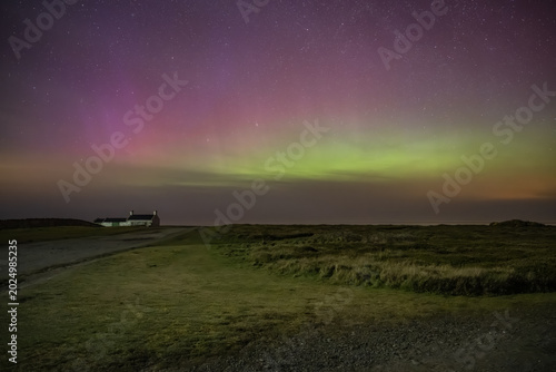 Shot at Point of Ayre, the northernmost point of the Isle of Man, this long exposure captures the glowing celestial phenomenon above the coastal landscape and a traditional stone wall.