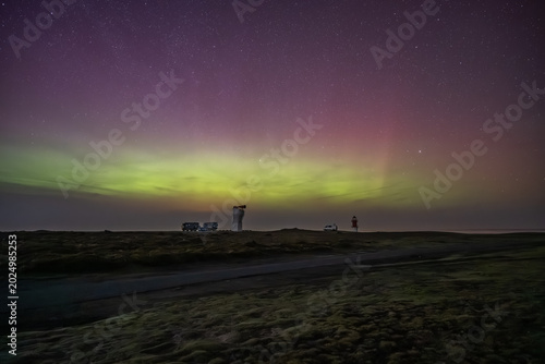 The historic white foghorn tower and the red-and-white Winkie Lighthouse stand under a vast night sky painted with green and pink Northern Lights,Point of Ayre, Isle of Man.