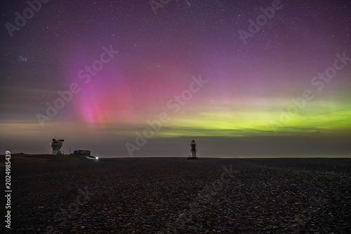 The historic white foghorn tower and the red-and-white Winkie Lighthouse stand under a vast night sky painted with green and pink Northern Lights,Point of Ayre, Isle of Man.