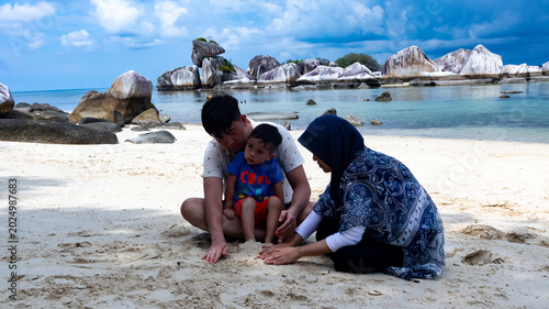 Photo of a small family on summer vacation playing in the sand on the beach on Belitung Island, Indonesia