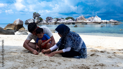 Photo of a small family on summer vacation playing in the sand on the beach on Belitung Island, Indonesia