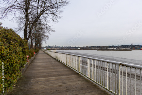 Riverside Boardwalk Promenade With Bare Trees And Distant City Skyline In New Westminster