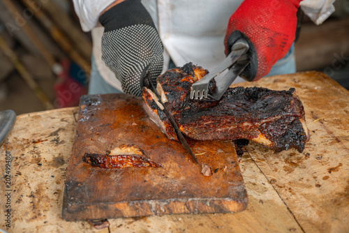 Fotografía Chef's hands wearing protective gloves slicing a large, well-done grilled meat p