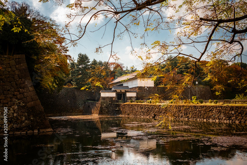 Fotografie Historic Japanese castle gatehouse reflected in moat surrounded by autumn foliag
