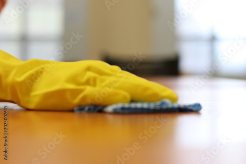 Woman hand in yellow glove holding a blue sponge on a wood background. Daily house cleaning and accessories to clean. Wood surface cleaning with soap and foam.