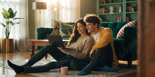 Young couple relaxing on rug looking at laptop in cozy living room