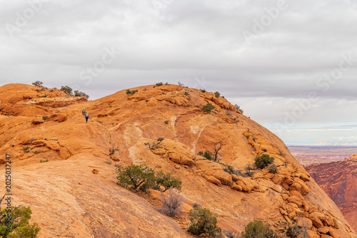 Slika na platnu Hikers ascend a rugged red rock mesa under an overcast sky.