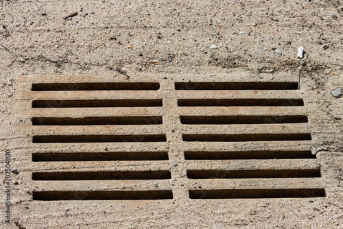 Tableau sur toile Quebec, Canada, 26 April 2026 : A metal grate is embedded in sandy ground with a discarded cigarette butt nearby