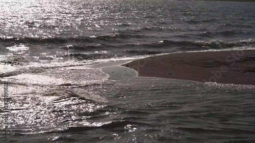A sandbar at a river mouth flowing into a bay, with the silhouette of distant mountain ranges in the background