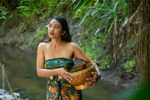 Картината върху платно Balinese woman in green floral strapless dress sitting in shallow river cradling