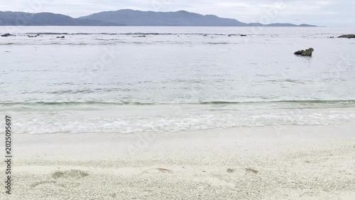 Serene Beach Landscape with Gentle Waves and Distant Mountains.