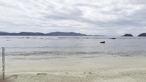 Serene Tropical Beach Landscape with Calm Ocean and Distant Islands Under Cloudy Sky.