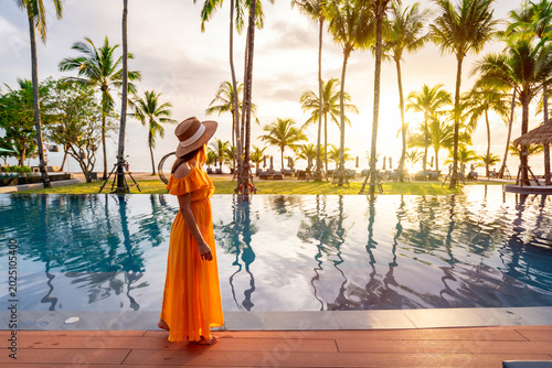 Female traveler enjoying the scenic palm tree reflection by the poolside at tropical resort, Sunset serene vacation vibes