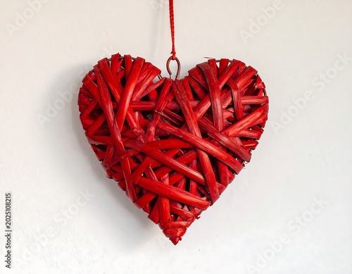 Bright Red Woven Heart Ornament Hanging on White Wall Background