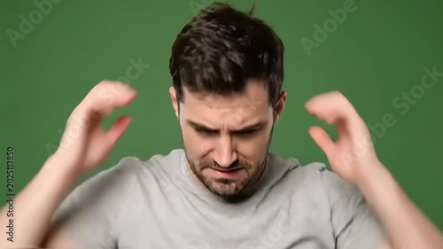 Young man feeling intense stress and frustration, holding his head with a worried expression against a vibrant green background, conveying anxiety and discomfort