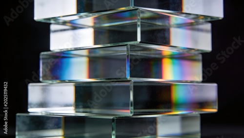 Abstract arrangement of stacked clear glass blocks with iridescent rainbow light refractions against a dark background.
