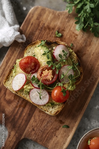 Delicious toast with avocado and vegetables on wooden board.